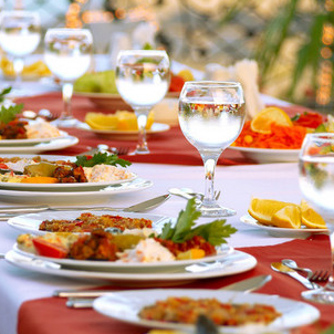 Diete per la collettività Tavola imbandita con piatti di cibo, bicchieri d'acqua e decorazioni festive.