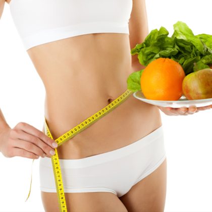 Dieta personalizzata Donna con addome snodato che tiene un piatto con frutta e verdura mentre misura la vita.